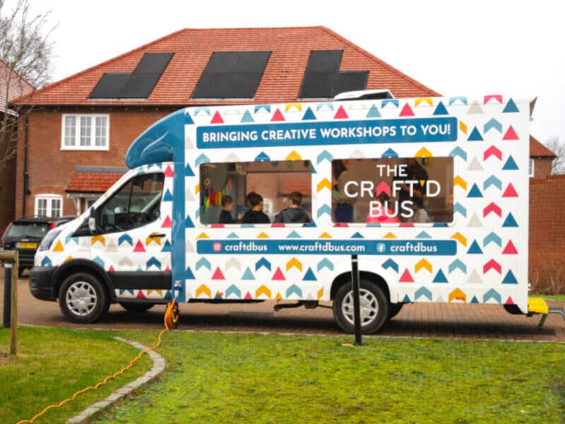 The custom craft bus, parked on a green with kids making artwork.